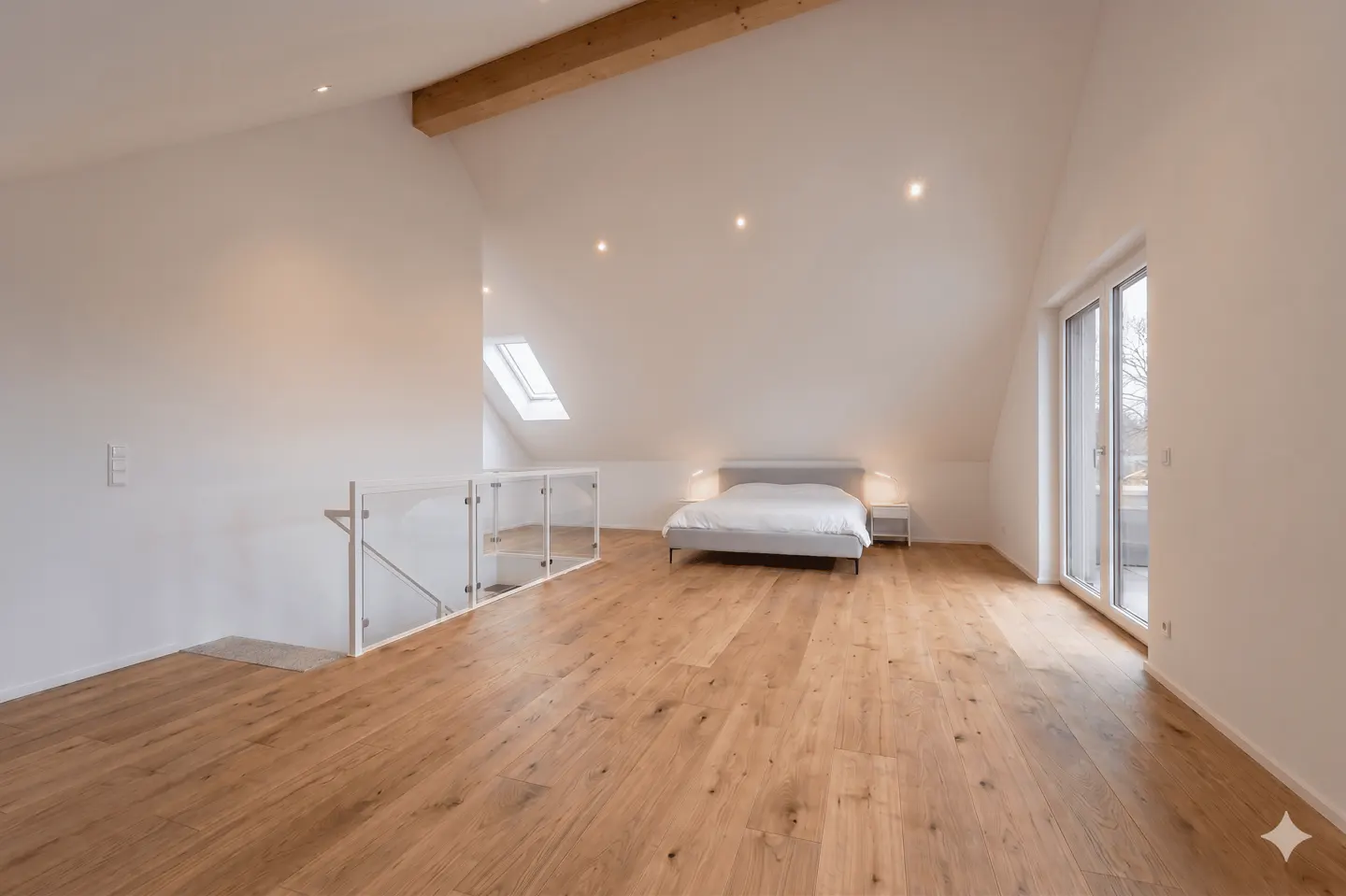 Bright, modern bedroom with wood floors, white walls, and a bed. A glass railing overlooks the lower level. A skylight and balcony door provide natural light.