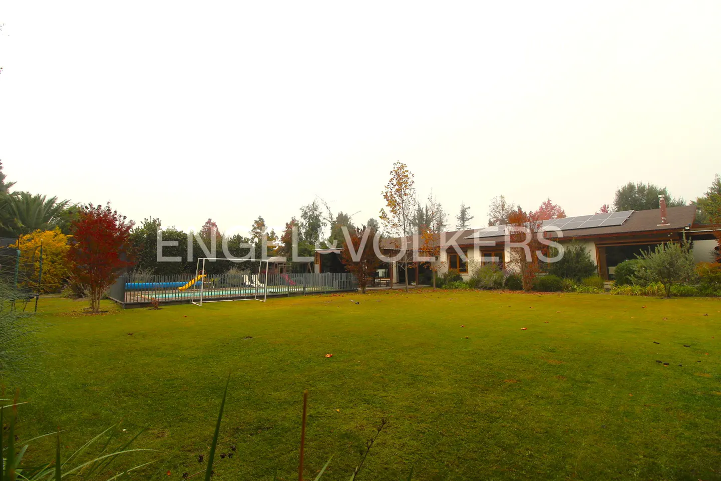 A wide shot of a house with a large green lawn, a pool, and trees. The house has solar panels on the roof.