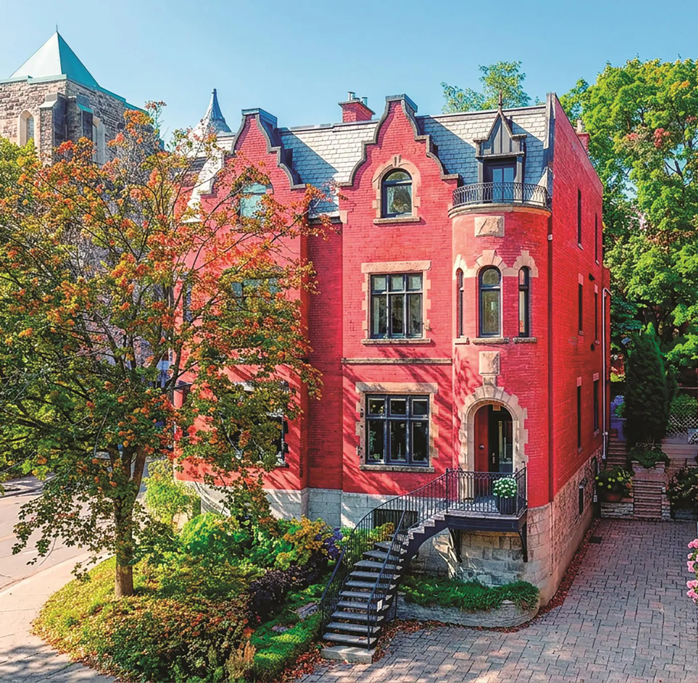 A three-story red brick house with black windows, a gray roof, and a stone foundation. A black staircase leads to the front door.