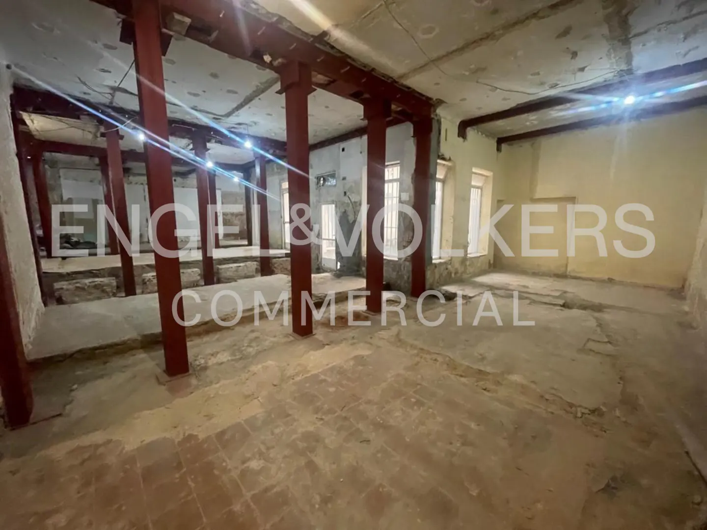 Spacious commercial space with red support beams, concrete floors, and natural light from windows. "Engel & Volkers Commercial" overlay.