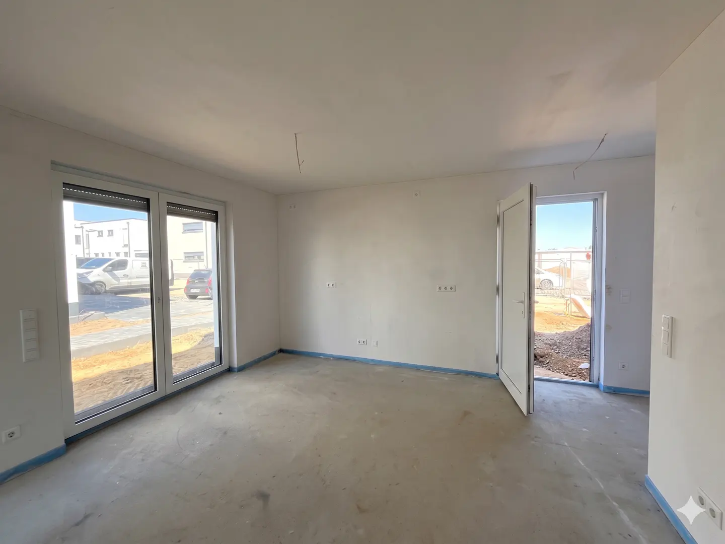 Unfinished room with white walls, concrete floor, and blue painter's tape. Sliding glass doors and an open white door lead outside.