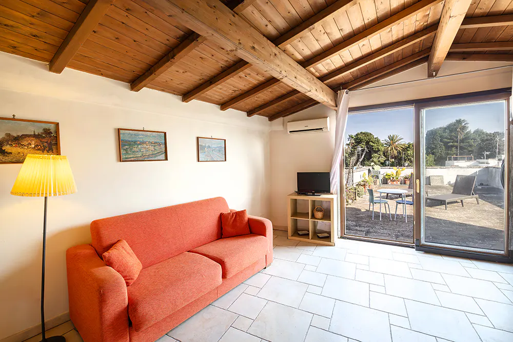 Living room with orange sofa, wood ceiling, and sliding glass doors to a patio with table, chairs, and lounge chair.