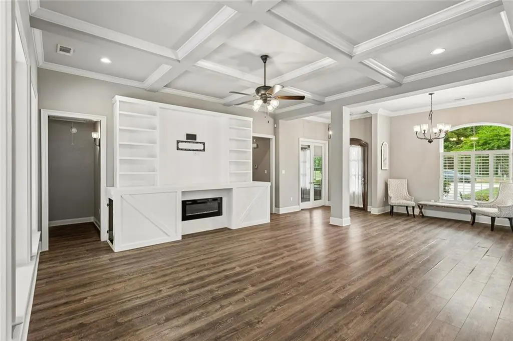 Spacious living room with wood floors, white built-in shelves, fireplace, and coffered ceiling with a ceiling fan.