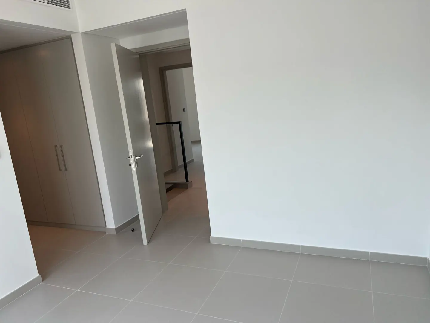 An empty room with gray tile floors, white walls, and a closet with two doors. A doorway leads to another room.