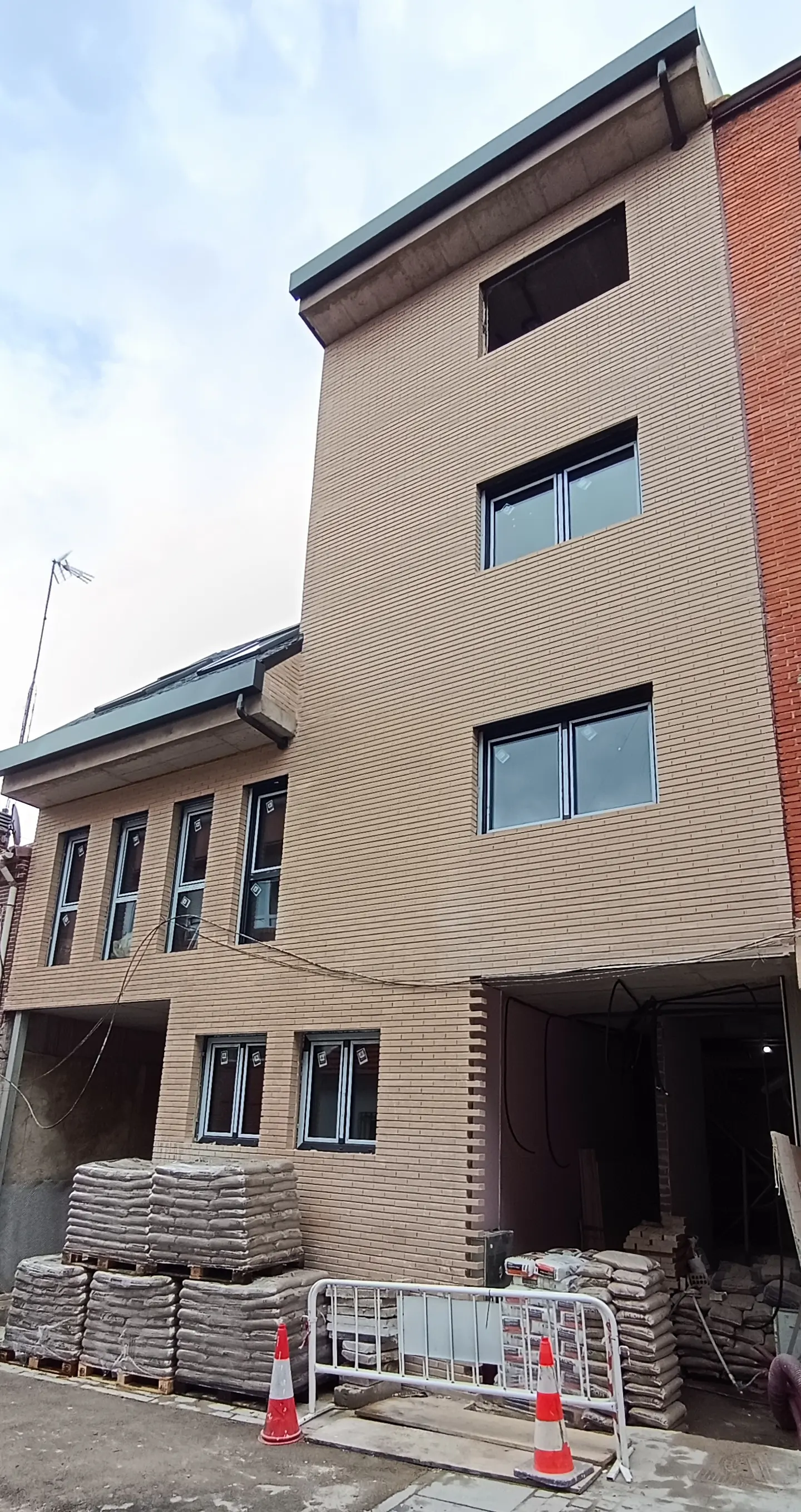 A beige brick building under construction with black-framed windows and stacks of materials outside.