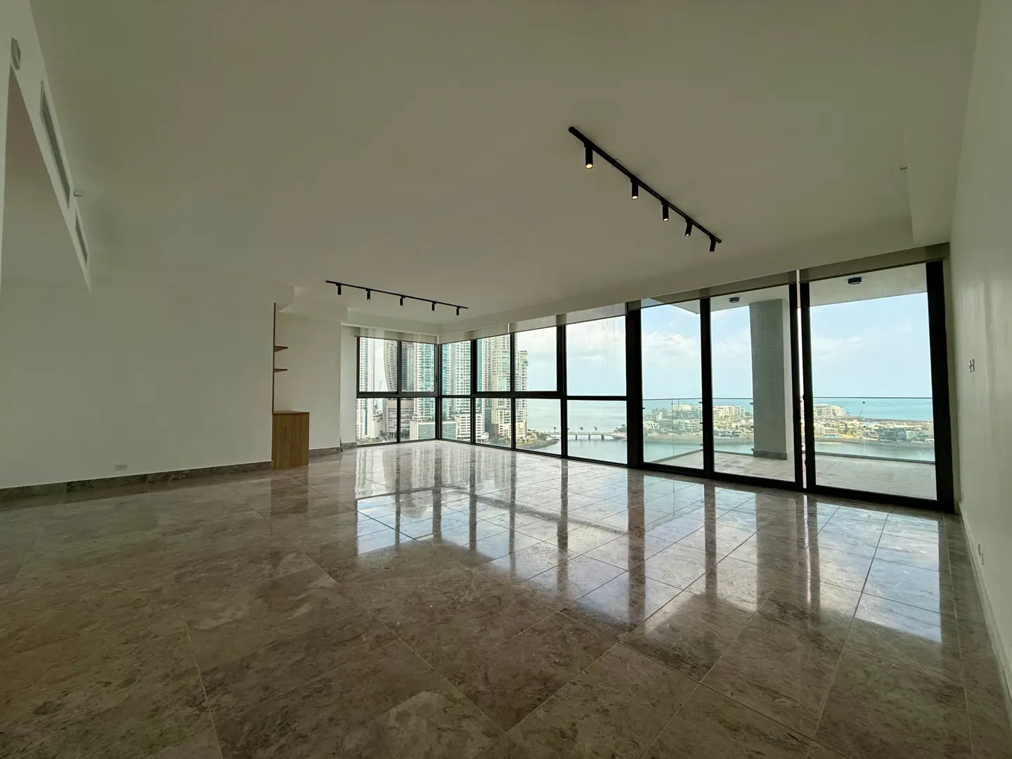 Empty, bright room with marble floors and floor-to-ceiling windows. City and ocean views. Track lighting on the ceiling.