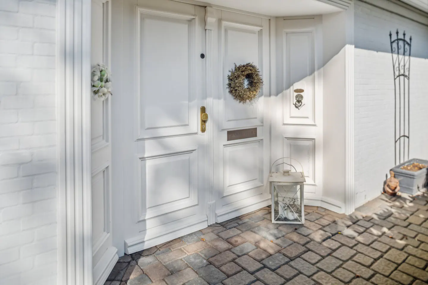 White double front door with a wreath, lantern, and brick walkway.