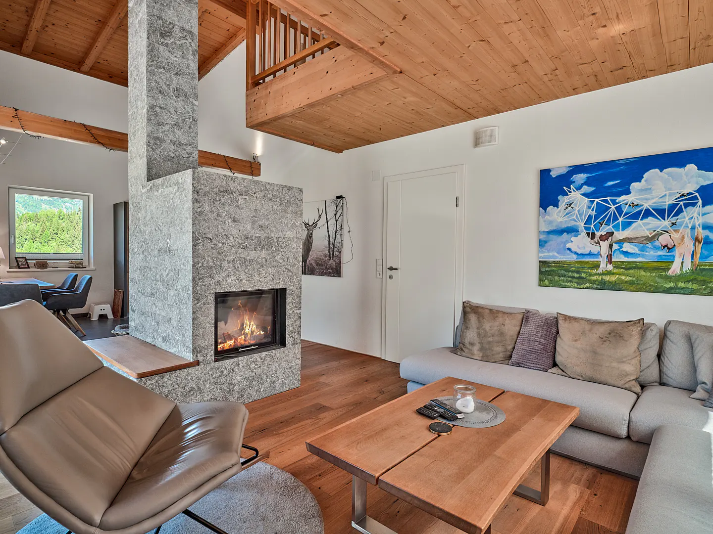 Living room with a stone fireplace, wood floors, and a gray sectional sofa. A painting of a cow hangs on the wall.