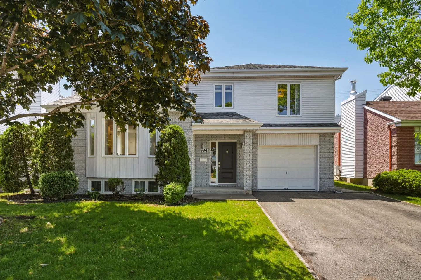 Two-story suburban home with light gray siding, a single-car garage, and a front lawn under a large tree on a sunny day.