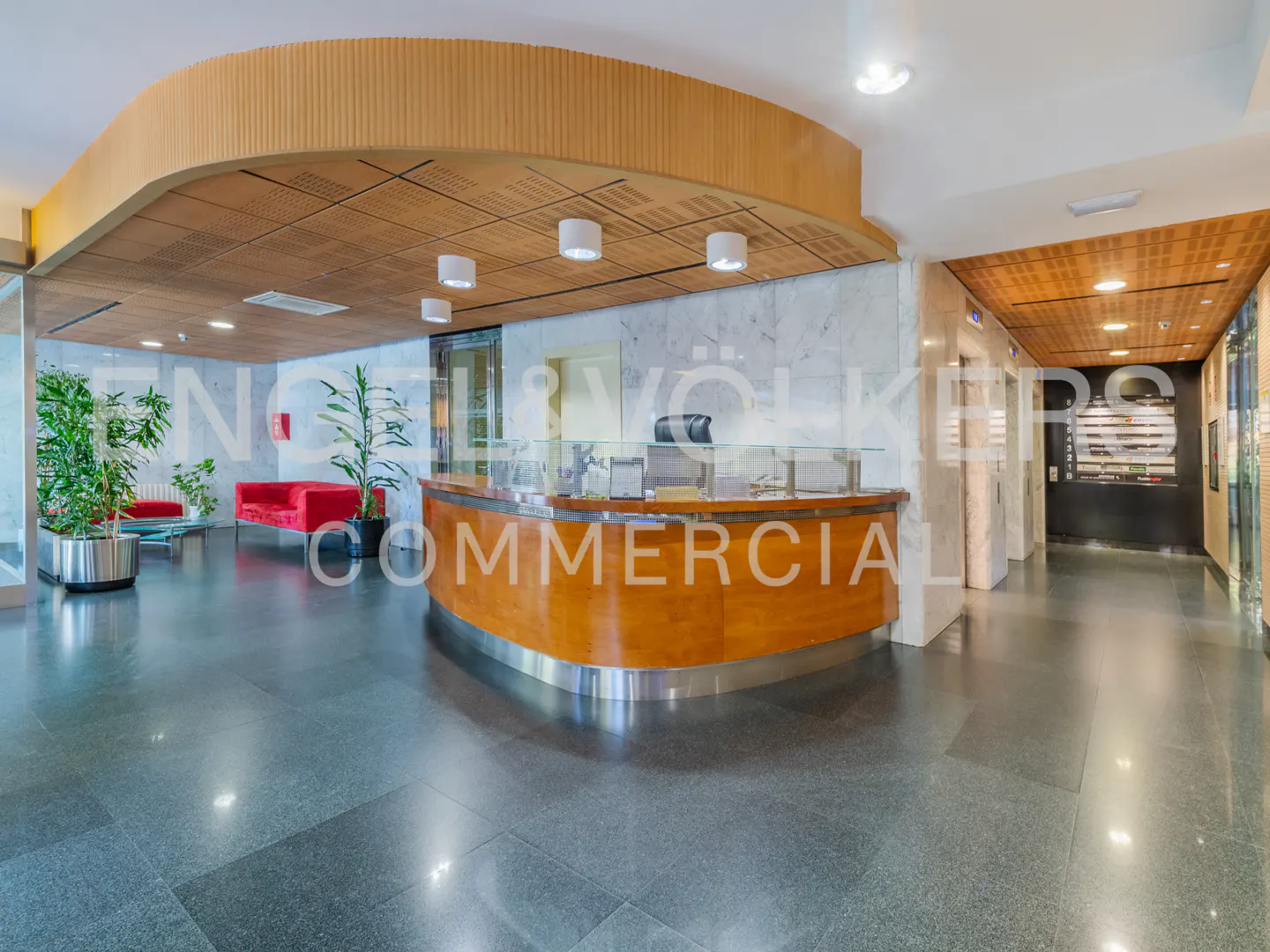 Office lobby with a curved wooden reception desk, marble walls, and a seating area with red sofas.
