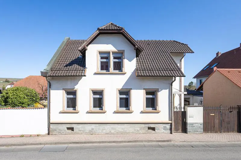 Two-story white house with a gray tiled roof and gray window frames on a sunny day.