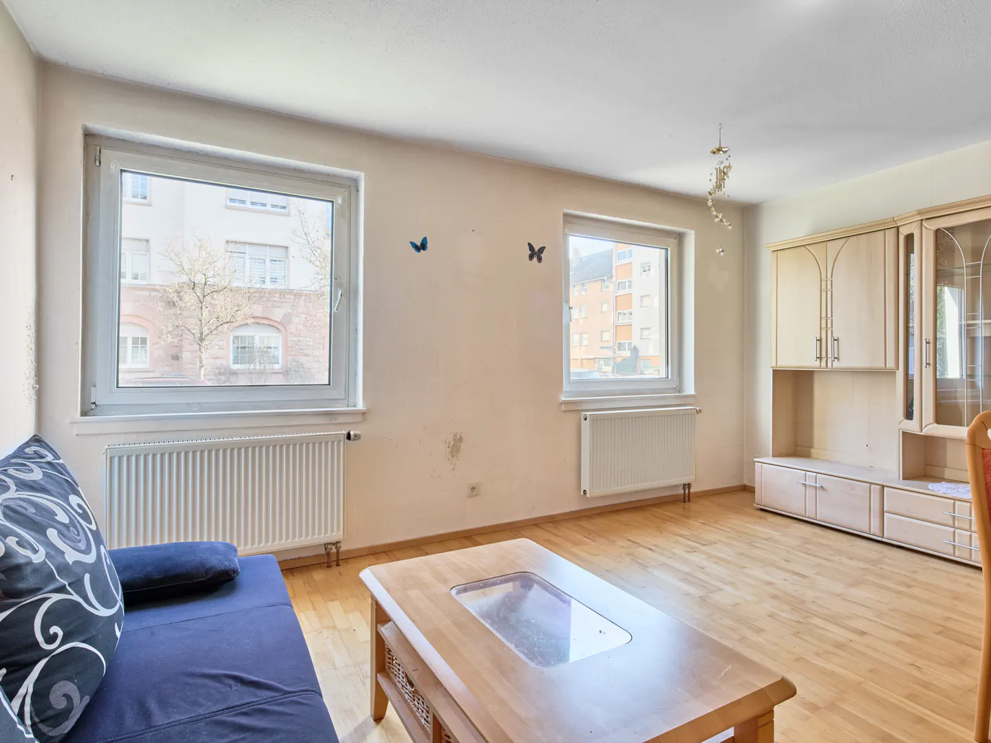 Bright living room with wood floors, two windows, blue sofa, wood table, and a light wood cabinet.