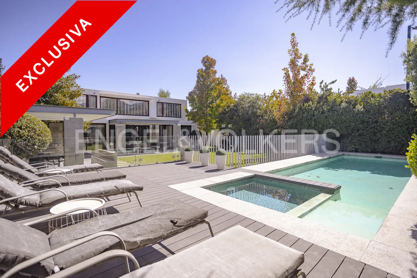 A modern house with a pool and lounge chairs on a sunny day. A red "Exclusiva" banner is in the upper left corner.