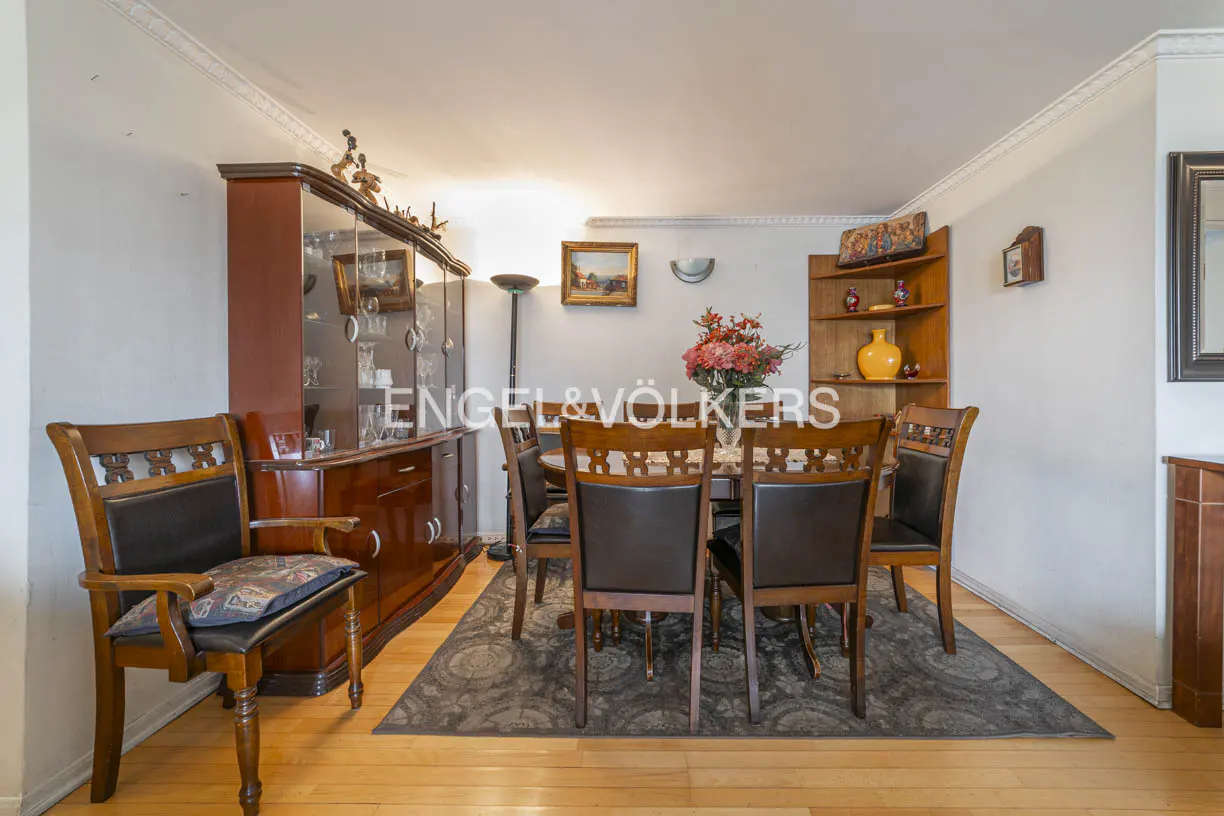 A dining room with a wooden table, chairs, and a china cabinet on a gray rug and wooden floor.