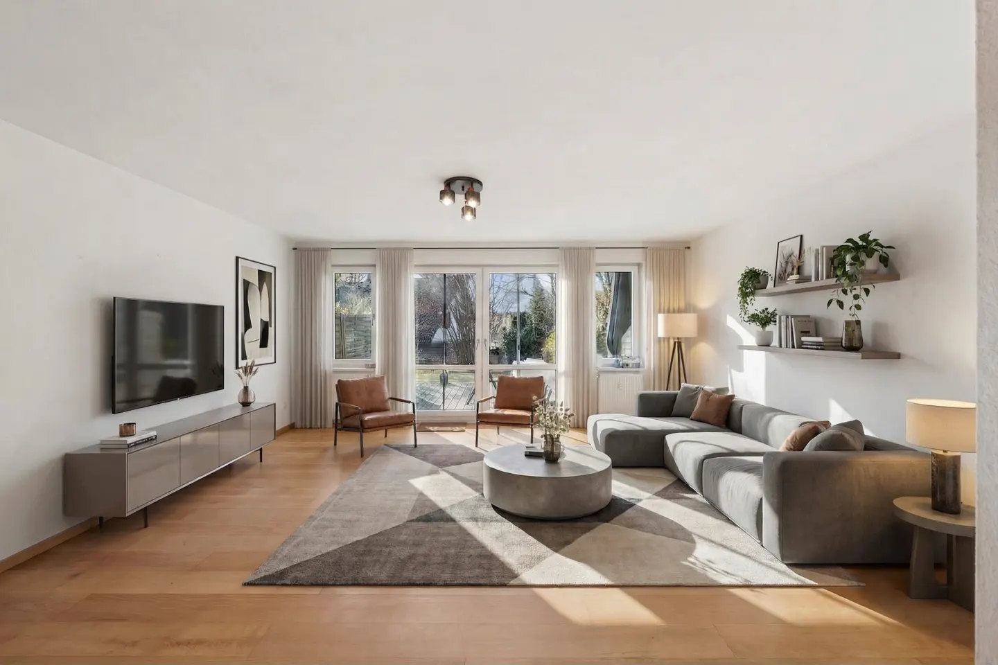 Bright living room with hardwood floors, a gray sectional sofa, and two brown leather chairs facing a large window.