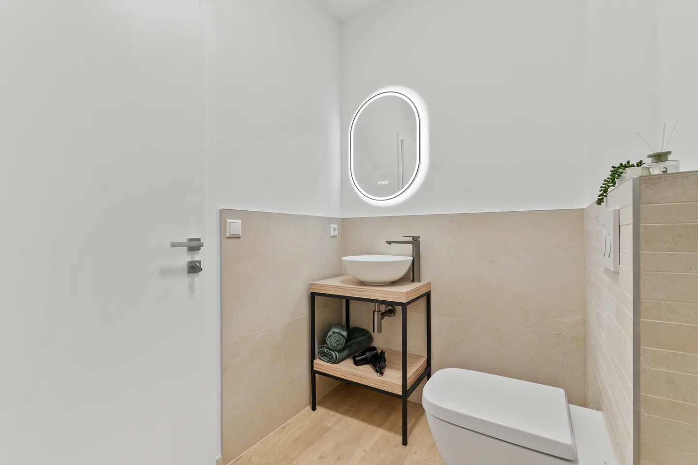 Bright bathroom with a white toilet, sink on a wooden stand, and a round mirror with a light.