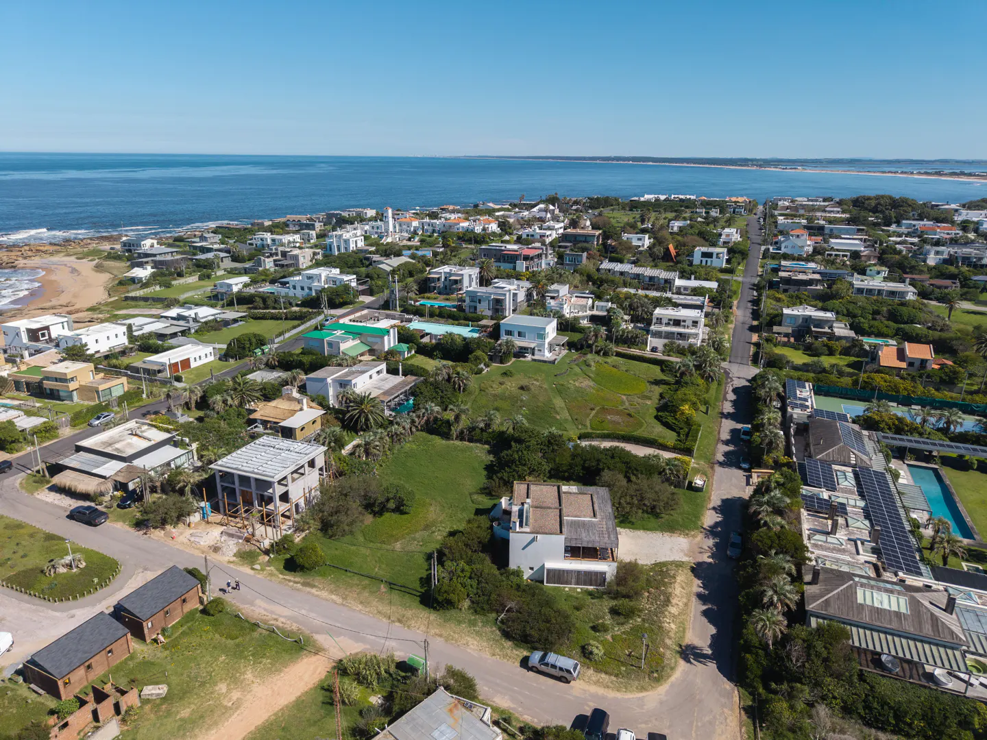 Aerial view of a coastal neighborhood with modern homes, green lawns, and the blue ocean in the background.
