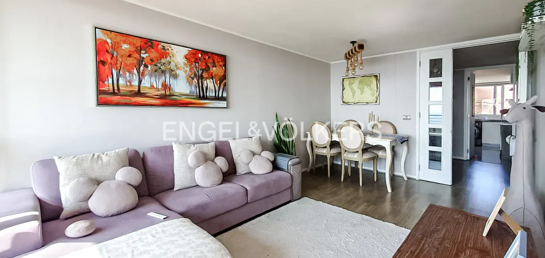 Living room with a purple sofa, Mickey Mouse pillows, a painting of trees, and a dining table with chairs.