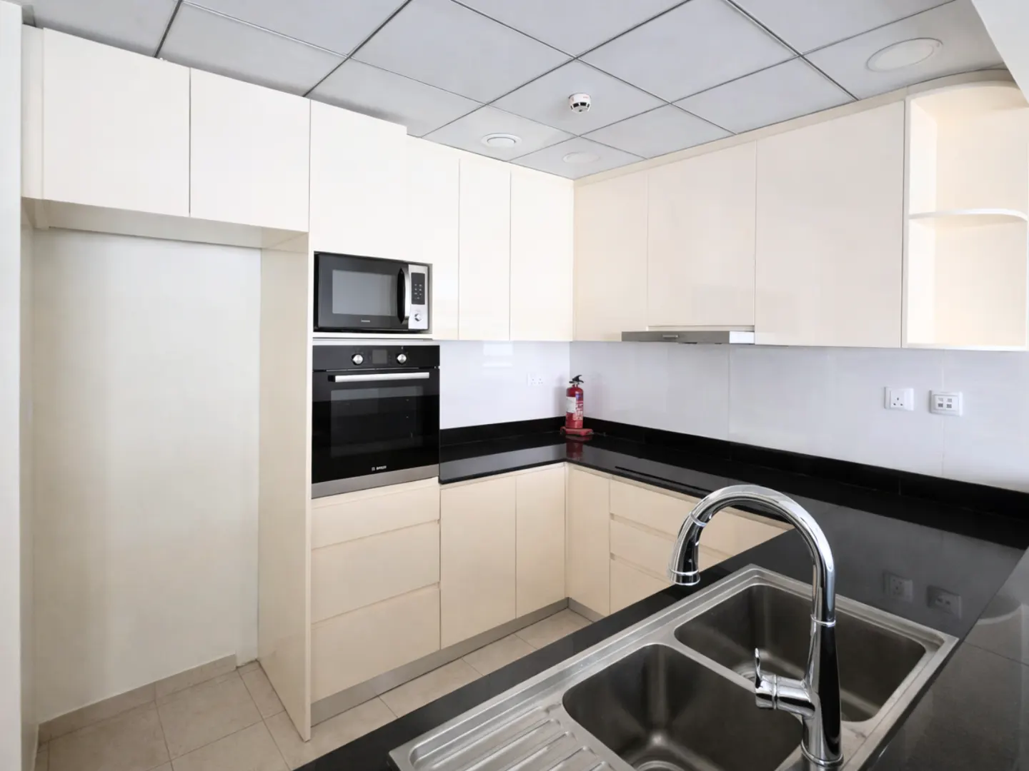 Modern kitchen with cream cabinets, black countertops, built-in oven, microwave, and a stainless steel double sink.