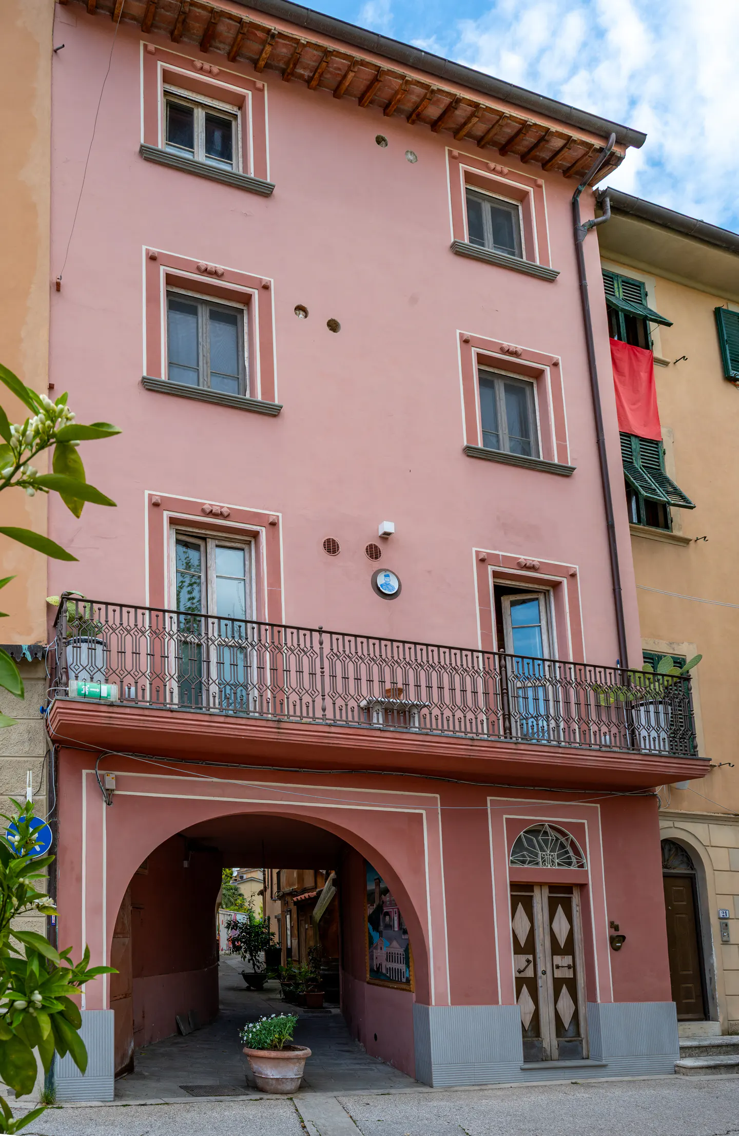 A three-story pink building with an arched passageway on the ground floor. A wrought iron balcony is on the second floor. Windows are framed in white.