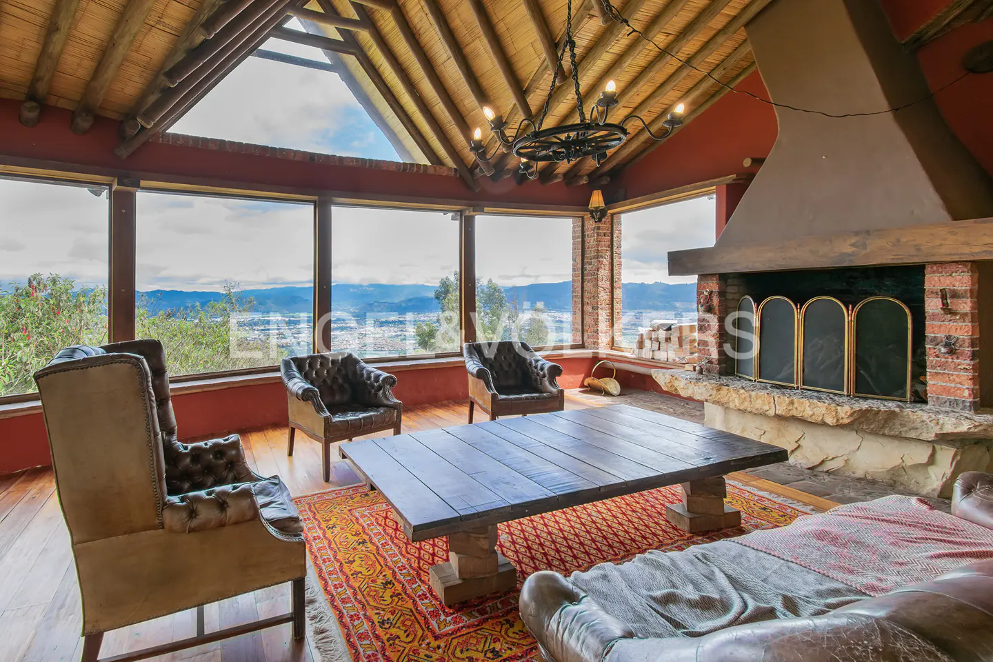 Rustic living room with leather armchairs, wooden coffee table, stone fireplace, and panoramic mountain views.