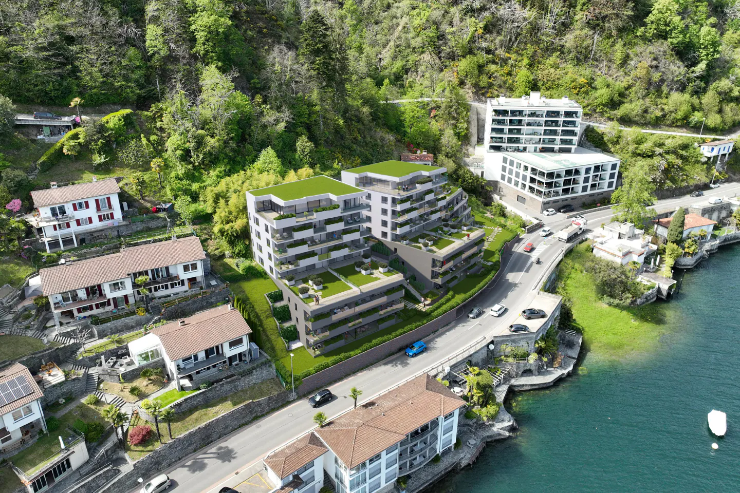 Aerial view of modern terraced apartment buildings nestled on a lush, green hillside overlooking a lake and coastal road.