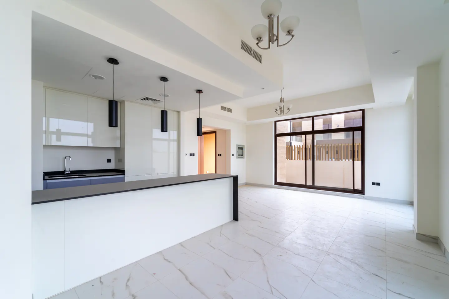 A bright, empty kitchen and living room with white marble floors and a large window.