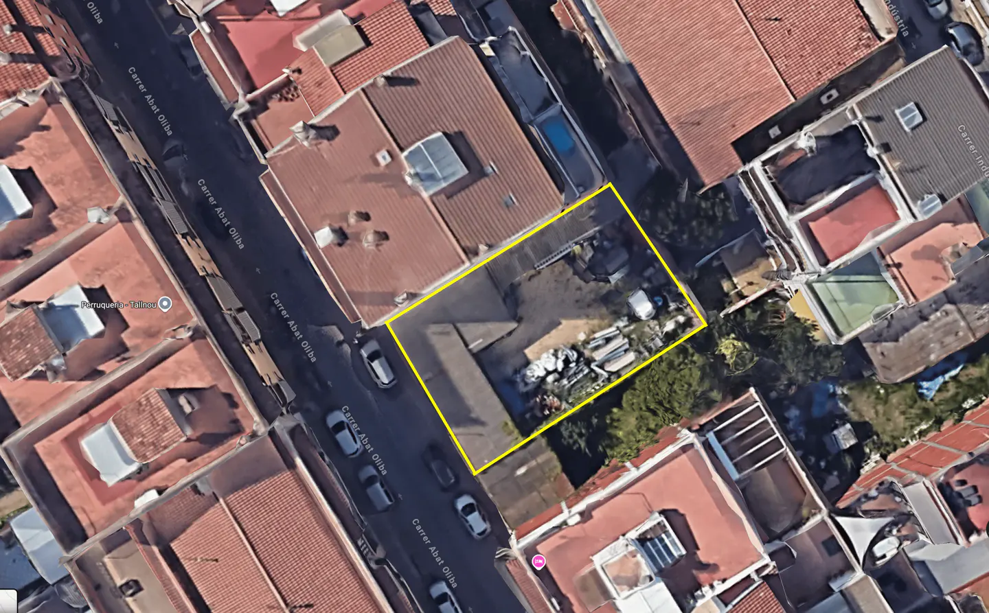Aerial view of a rectangular urban plot outlined in yellow, situated between residential buildings with red-tiled roofs.