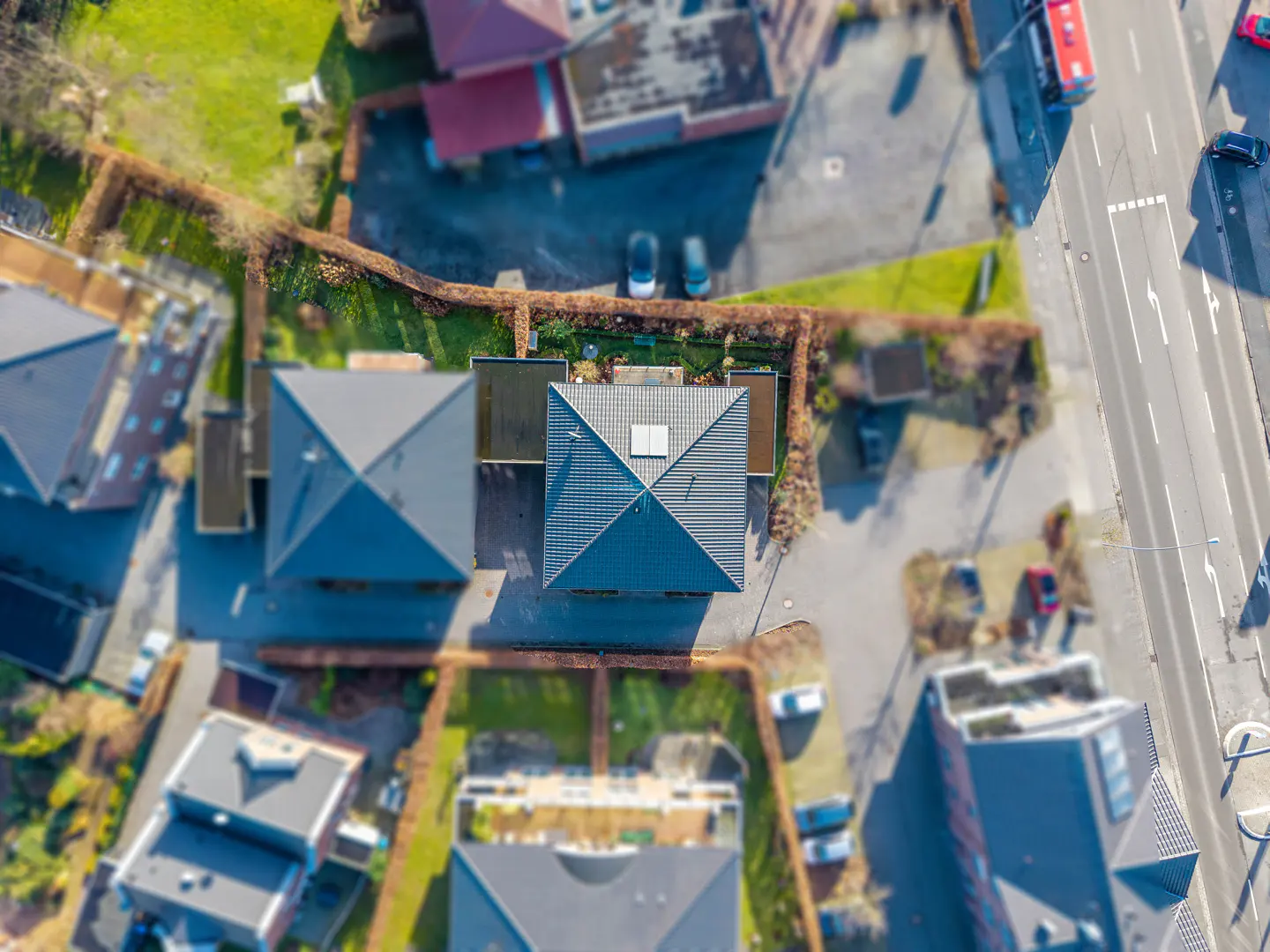 Aerial view of a neighborhood with houses, green lawns, and a street with cars. The houses have gray roofs.