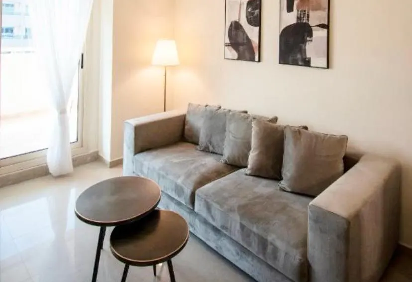 Modern living room with a grey sofa, two round nesting coffee tables, a floor lamp, and abstract art on a beige wall.