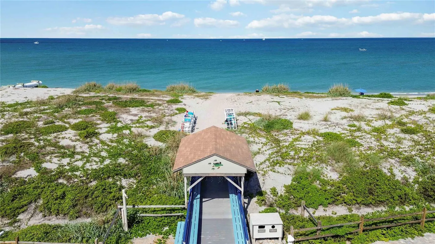 Beach access with a blue boardwalk leading to the sand and ocean. Green vegetation covers the dunes.