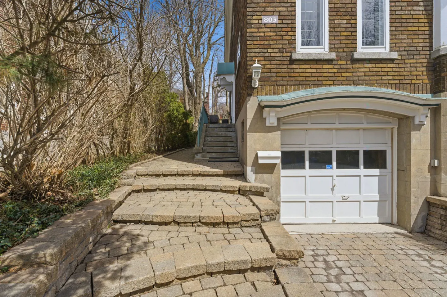 Exterior view of a brick house with a white garage door and stone steps leading to the front door.