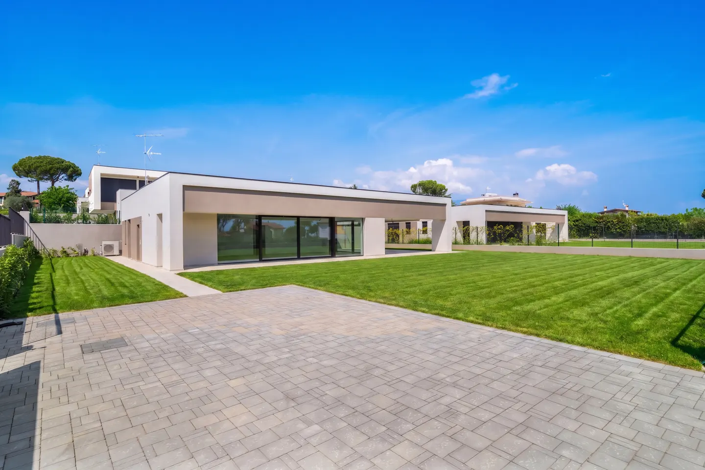 Modern white house with a gray driveway, green lawn, and blue sky.
