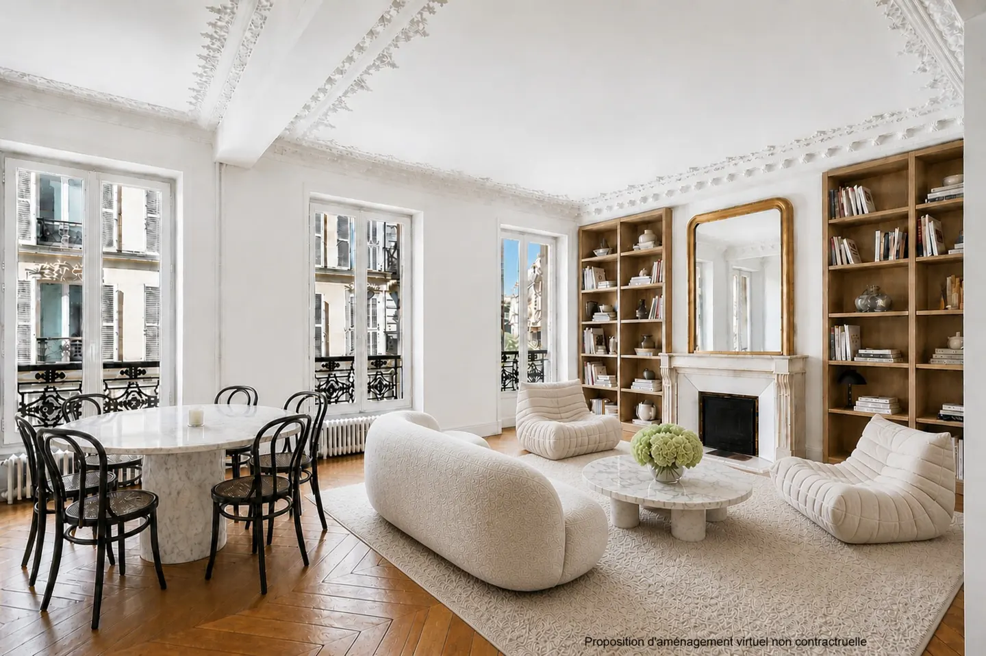 Bright living room with white walls, herringbone wood floors, and ornate ceiling molding. A marble table with black chairs sits near large windows. A white sofa and chairs surround a marble coffee table. Built-in bookshelves flank a fireplace.