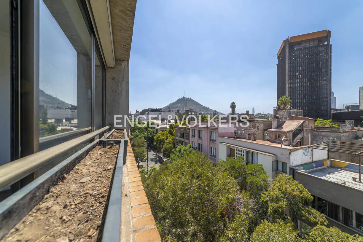 View from a balcony with empty planters, overlooking a city with a tall building and a mountain in the background.