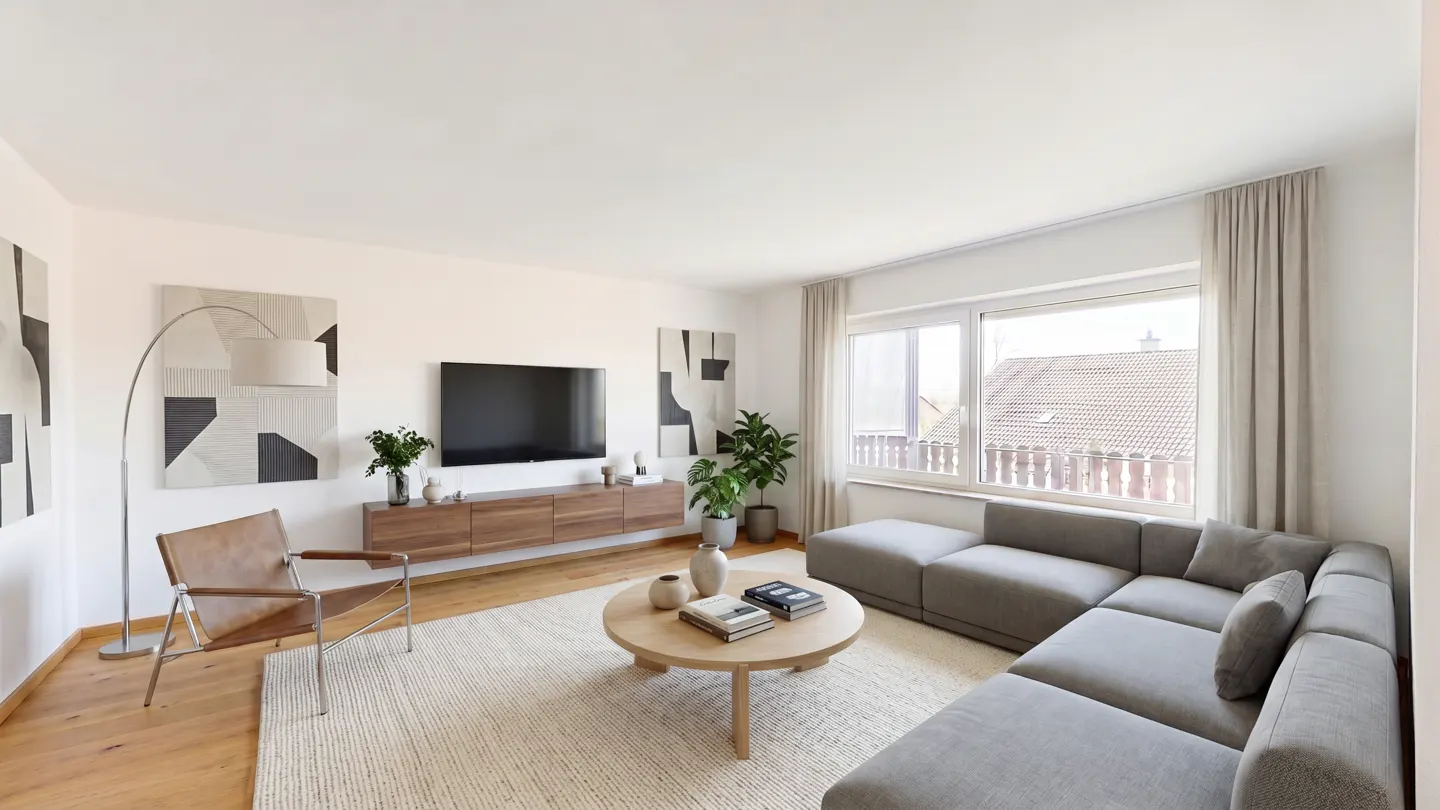 Bright living room with a gray sectional sofa, round wood table, and a large window with curtains. A TV is mounted above a wood console.