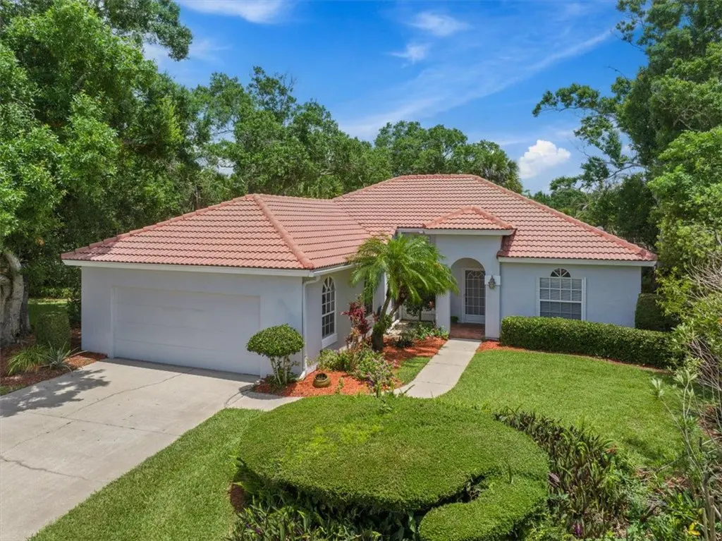 A single-story house with a red tile roof, light gray exterior, and green landscaping on a sunny day.