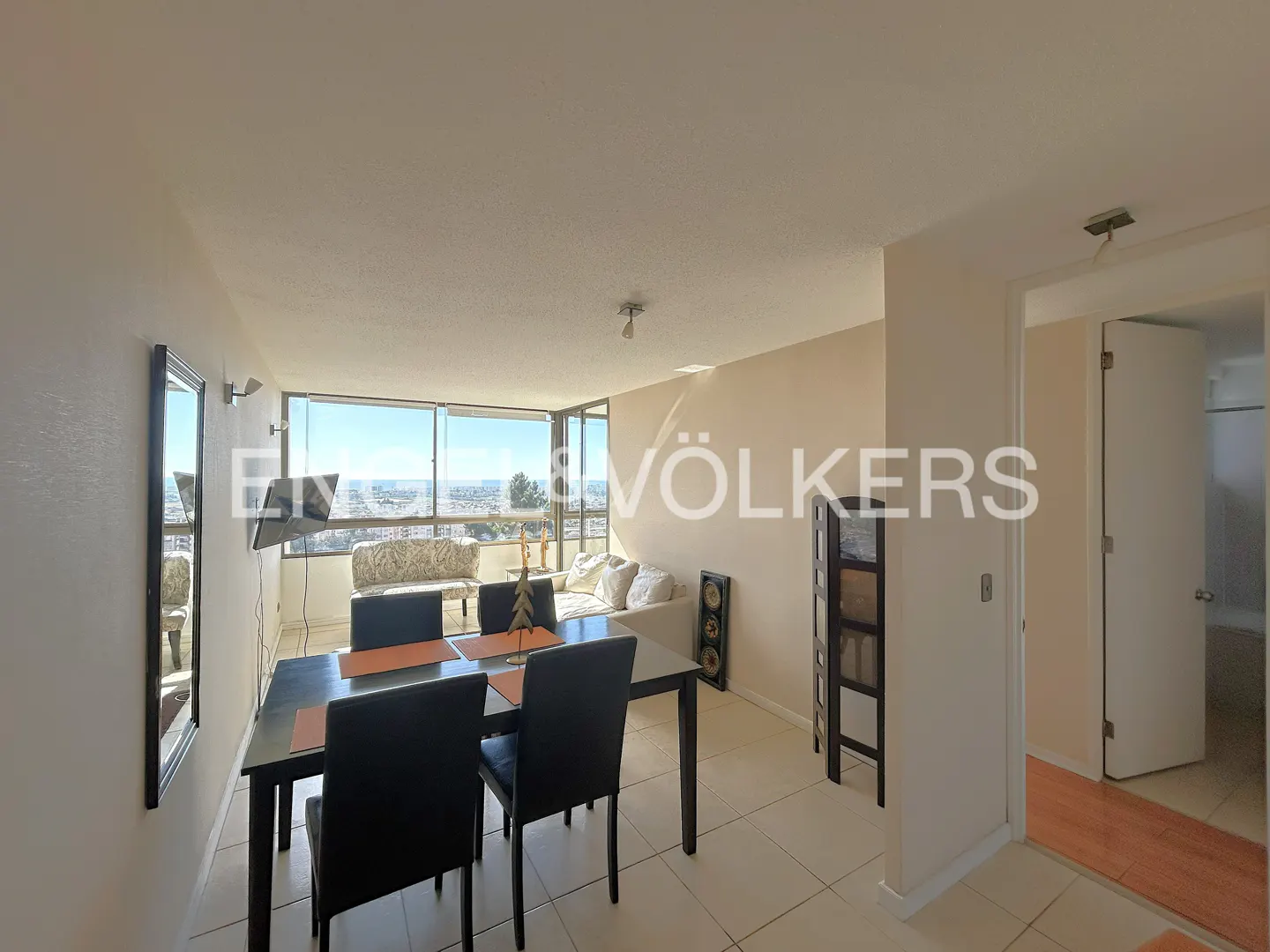A bright apartment interior with a dining table, chairs, and a view of the city through a large window.