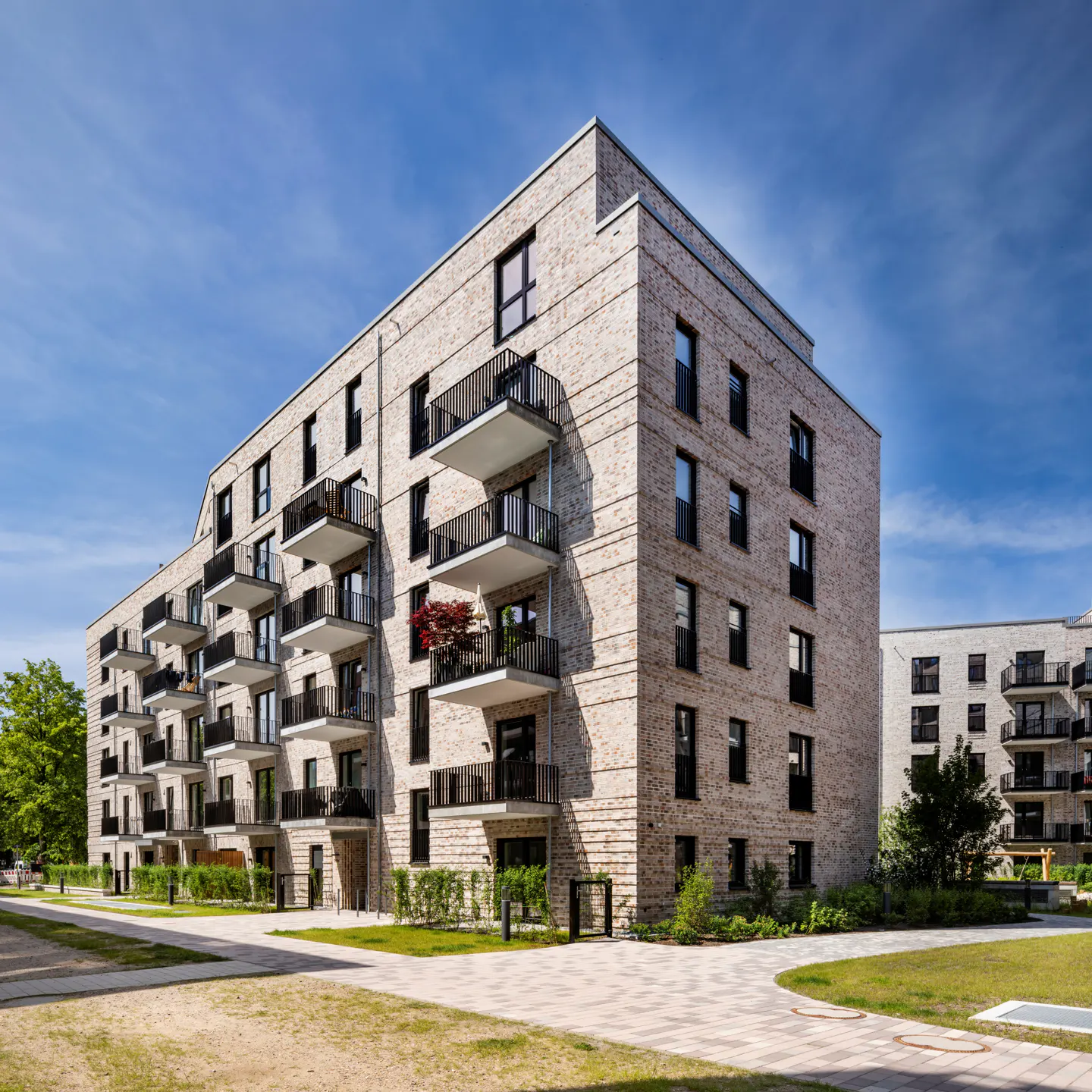 Exterior view of a modern brick apartment building with black balconies under a blue sky.