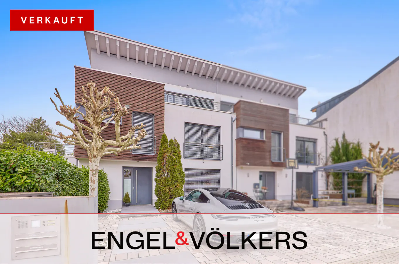 Modern townhouse with a white Porsche parked in front. "Verkauft" banner in the upper left corner. Engel & Völkers logo at the bottom.
