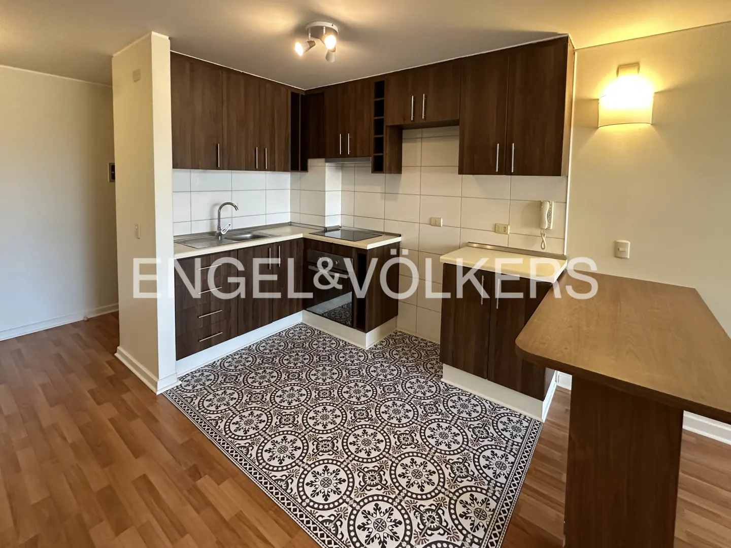 A kitchen with dark wood cabinets, white tile backsplash, and patterned floor. A small table is on the right.