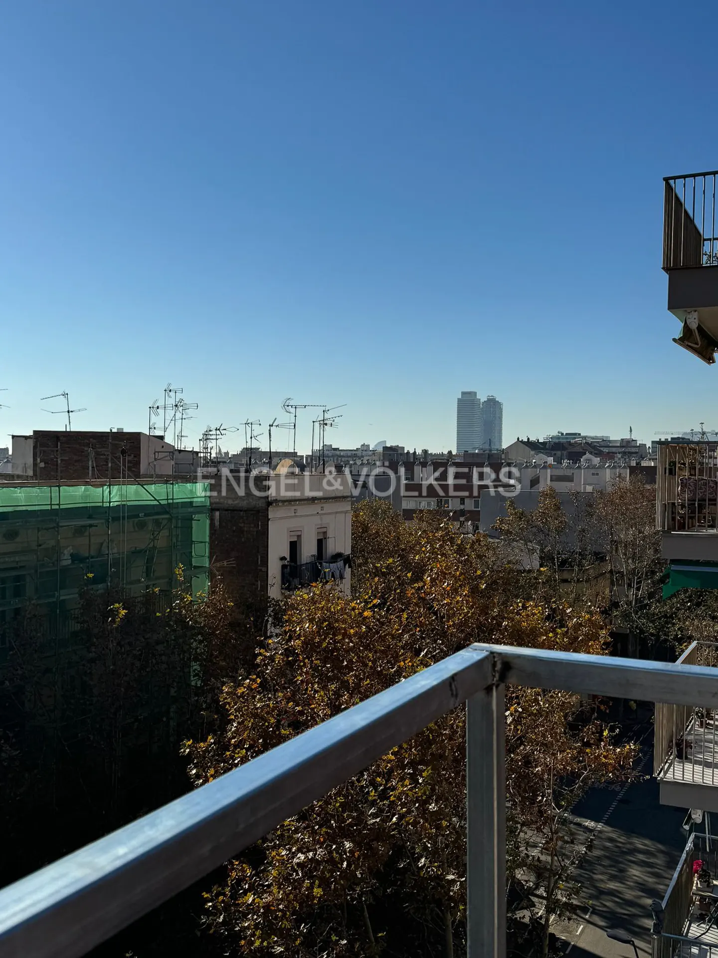 View from a balcony with a metal railing overlooking a city skyline under a clear blue sky. Engel & Volkers logo is visible.