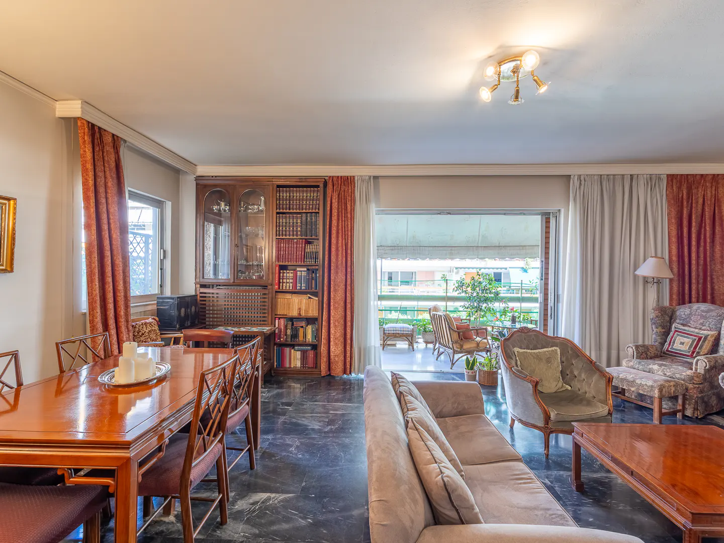 Spacious living and dining room with marble floors, wooden furniture, a bookshelf, and a balcony view.