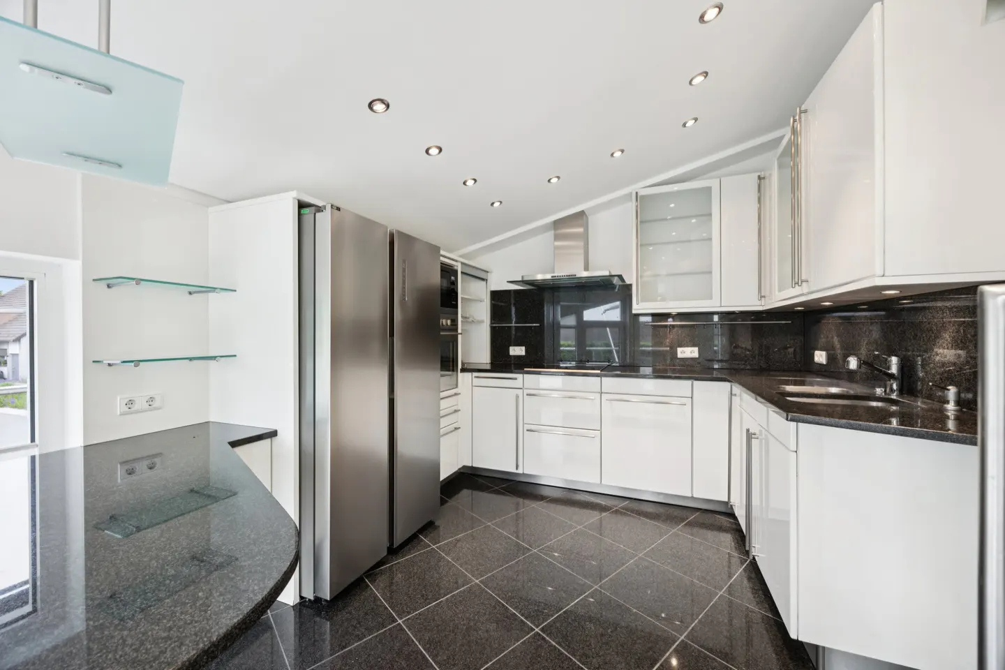 A modern kitchen with white cabinets, black granite countertops, and a stainless steel refrigerator. The floor is black tile.