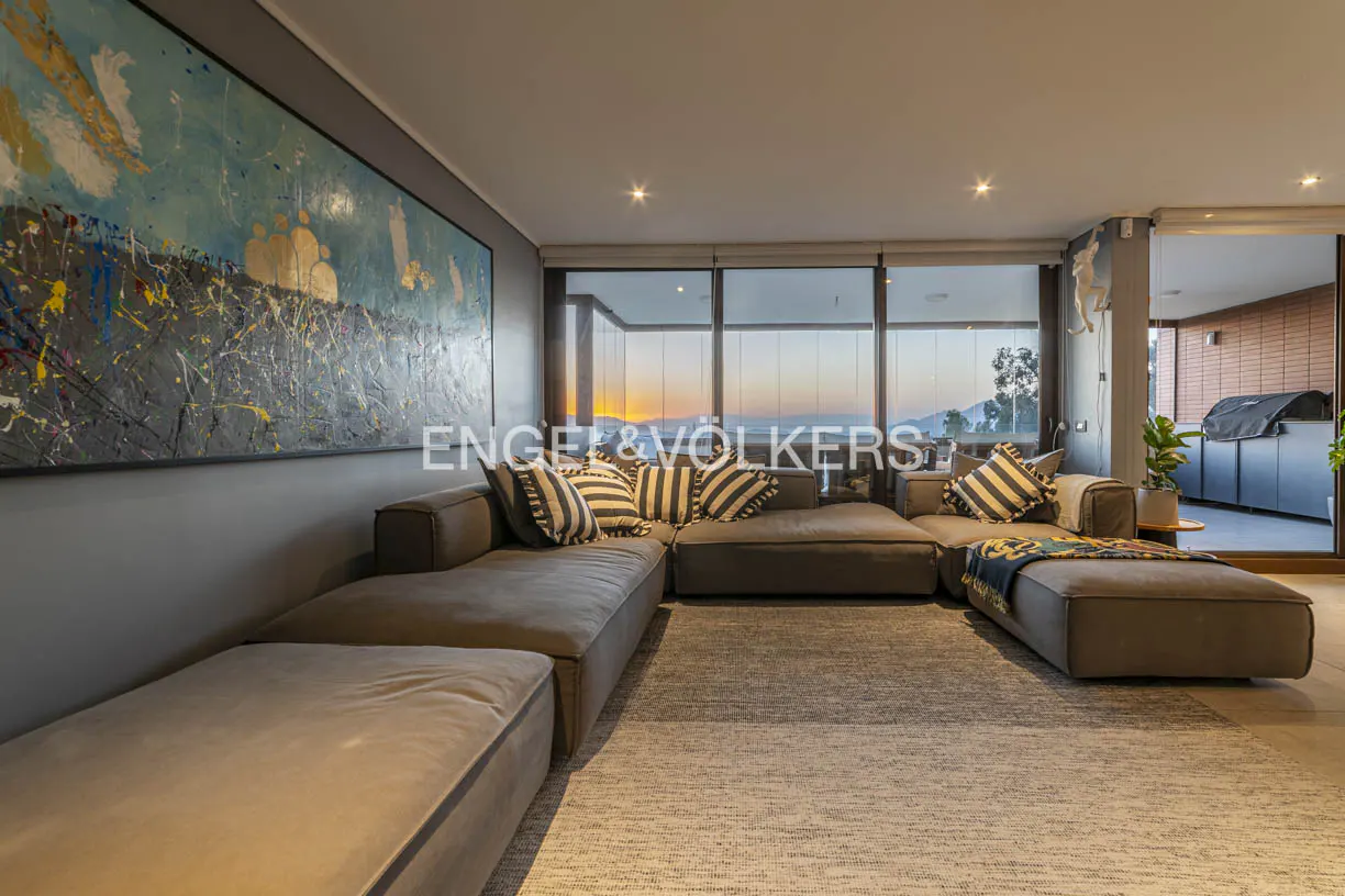 Living room with a large gray sectional sofa, striped pillows, and a colorful abstract painting. Sunset view through the windows.