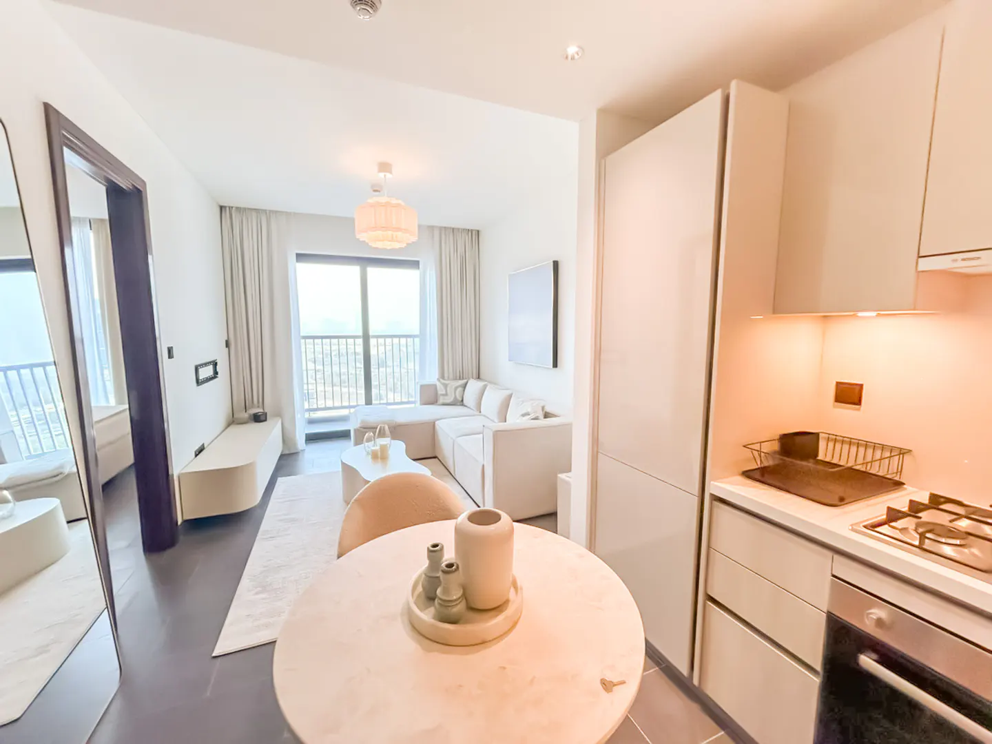 Modern open-plan apartment with a round dining table, cream sofa, and sleek kitchen featuring light-toned cabinetry.