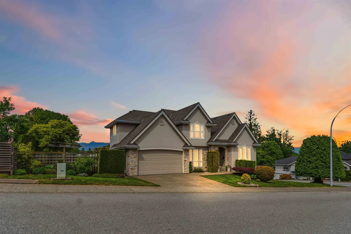 Two-story gray house with a gray roof, a garage, and green landscaping at sunset.