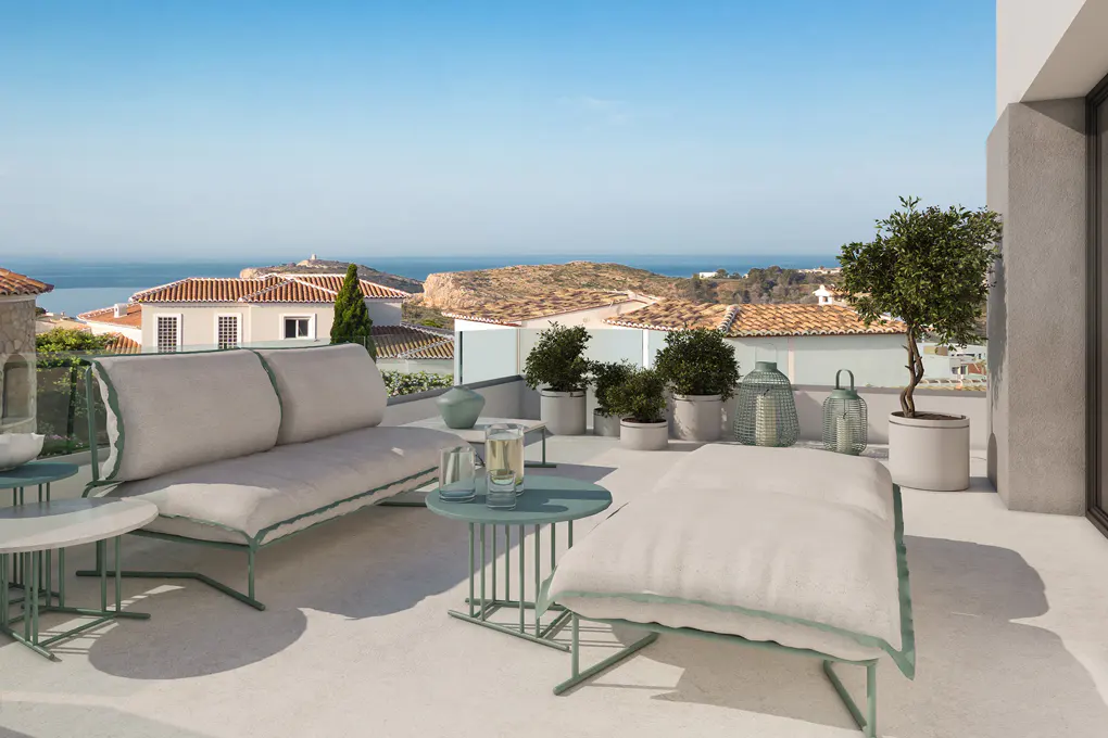 Outdoor patio with sofa, ottoman, and tables overlooking ocean and coastal town on a sunny day.