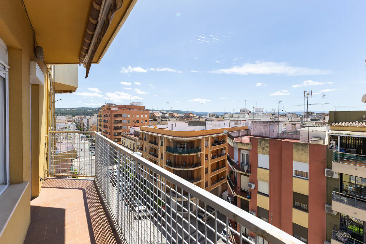View from a balcony with a metal railing overlooking a city with orange and white buildings under a blue sky.