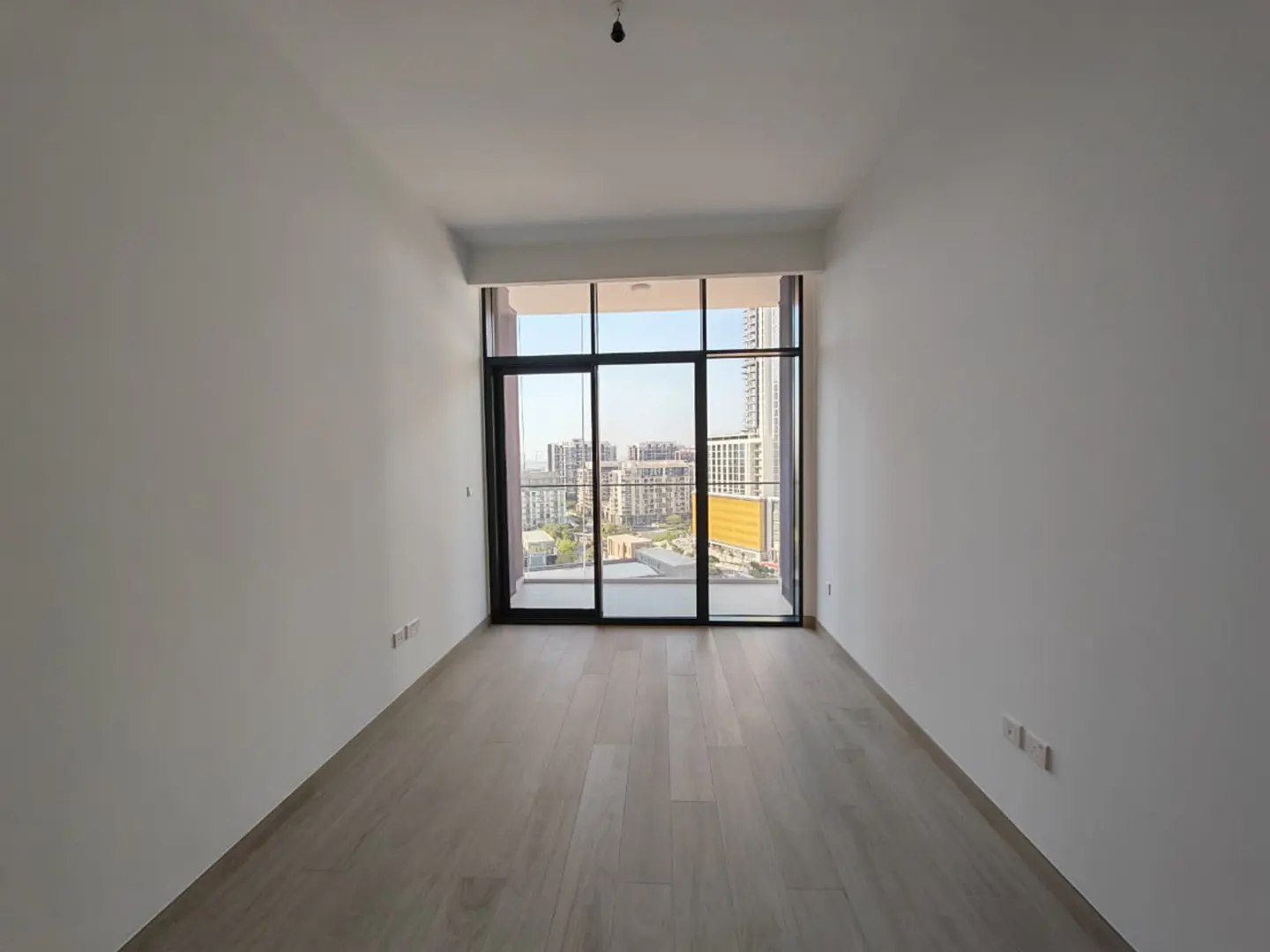 Empty room with light wood floors and white walls. Large window with a city view.